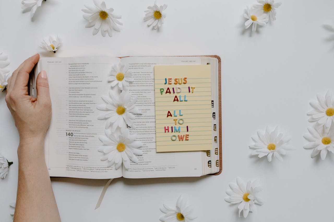 Crafting Captivating Headlines: Your awesome post title goes here Open Bible with daisies and a note saying 'Jesus paid it all' creating a peaceful setting.